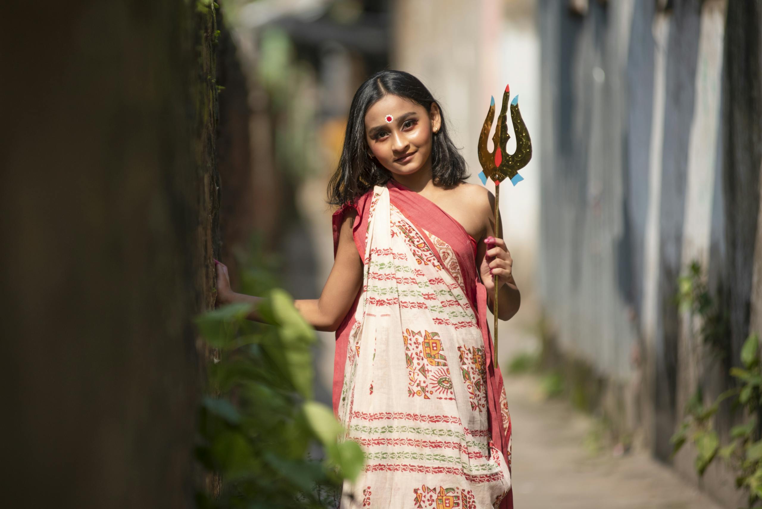 A young girl in traditional wear poses in an alley, capturing cultural authenticity with a warm smile.