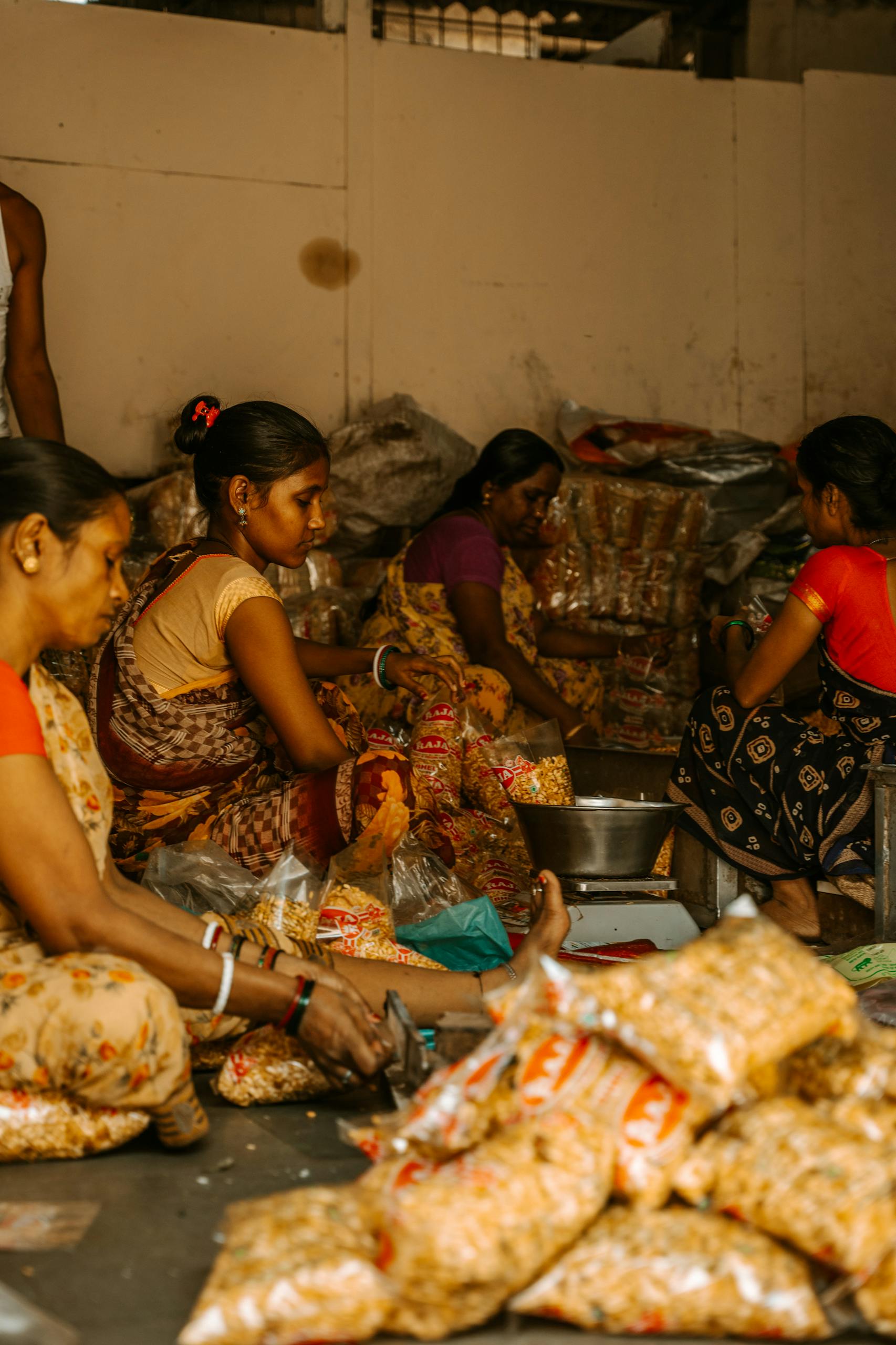 Indian women sorting and packaging snacks in an indoor village setting.